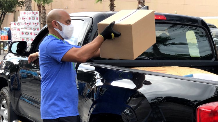 Man wearing a face mask load box of food into black pick up truck. 