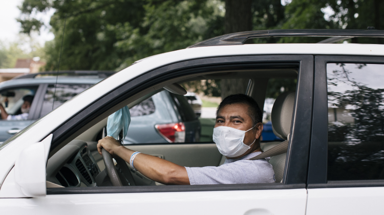 A man wearing a mask waits in his car to receive food at a mobile food distribution. 