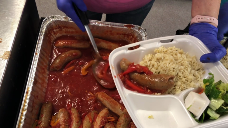 A volunteer serves a meal of sausages and peppers, rice and salad. 