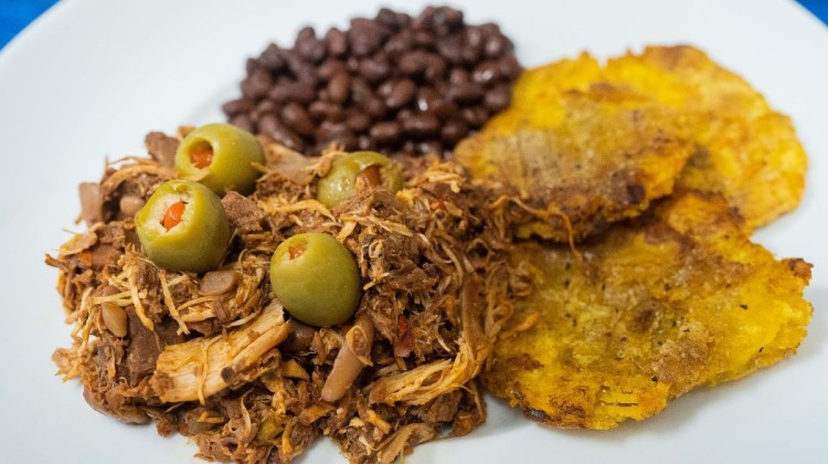 Photo of ropa vieja served with green olives, fried plantains and black beans.